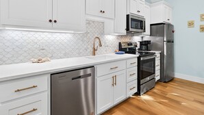 A modern kitchen with white cabinetry, a stainless steel dishwasher, a built-in oven, and a refrigerator. - Sea Esta F601b 2 Bedroom Home (Fulton)