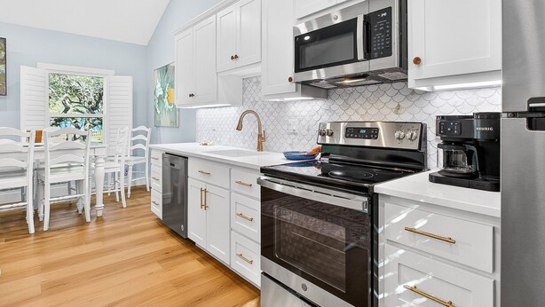 A modern kitchen with white cabinetry, stainless steel appliances, and a wooden floor. - Sea Esta F601b 2 Bedroom Home (Fulton)
