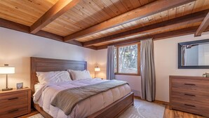 A bedroom with a wooden ceiling, a large bed, bedside tables, a dresser, and a window with curtains. - Dollar Point - Observation Dr. 3 Bedroom Home (Tahoe City)