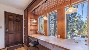 A room with a wooden desk, two pendant lights, a chair, and large windows with a view of snow-covered trees. - Dollar Point - Observation Dr. 3 Bedroom Home (Tahoe City)