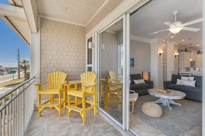 A balcony with yellow Adirondack chairs, a glass door leading to a living area with a gray sofa, a round coffee table, and a ceiling fan. - 1947 S Fletcher 2 Bedroom Townhouse (Fernandina Beach)