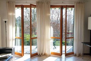 Een kamer met een schuifdeur met glas dat uitkomt op een balkon, een zwarte leren bank en een tafel met een lamp.