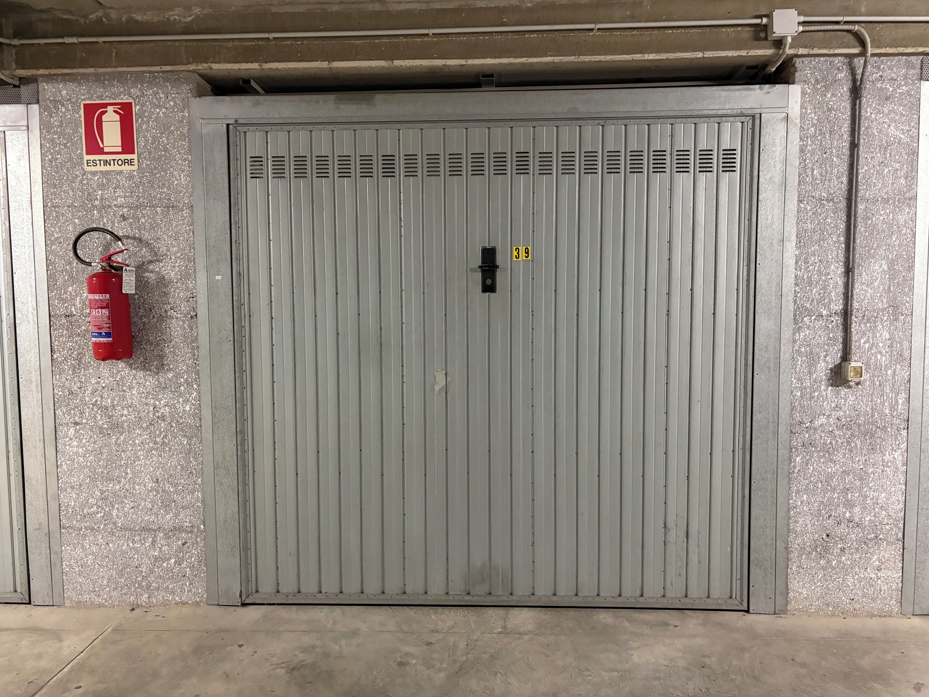 Puerta metálica gris con extintor y señalización de salida de emergencia.
