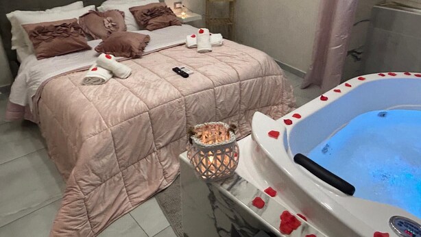Un dormitorio con cama, mesita de noche, luz empotrada en la pared y baño con bañera.