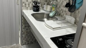 Una cocina con cubierta blanca, un lavamanos, un escurreplatos y una estufa.