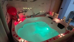 Un jacuzzi con luz azul turquesa, rodeado de pétalos de rosa y un globo rojo.