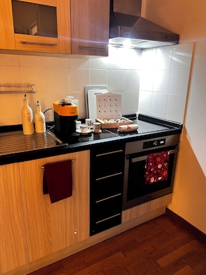 A compact kitchen with wooden cabinets, a black countertop, a stainless steel oven, and a coffee machine. - The Sommelier's Stop Romantic & Wine (Firenze)