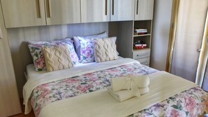 Un dormitorio con cama, ropa de cama estampada, cabecero, armario y mesita de noche con libros.