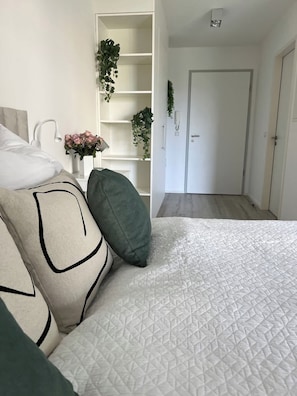 Un dormitorio moderno con una colcha blanca acolchada, un cabecero blanco y una mesita de noche con un jarrón de flores.
