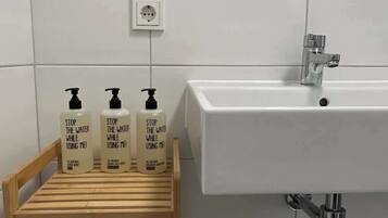 Ein Badezimmer mit einem weißen Waschbecken, einem Spiegel darüber und drei Seifenflaschen auf einem Holzboden.