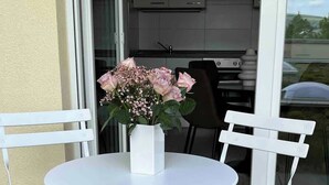 Une table et des chaises en métal blanc sont disposées sur une terrasse, avec un vase blanc rempli de fleurs.