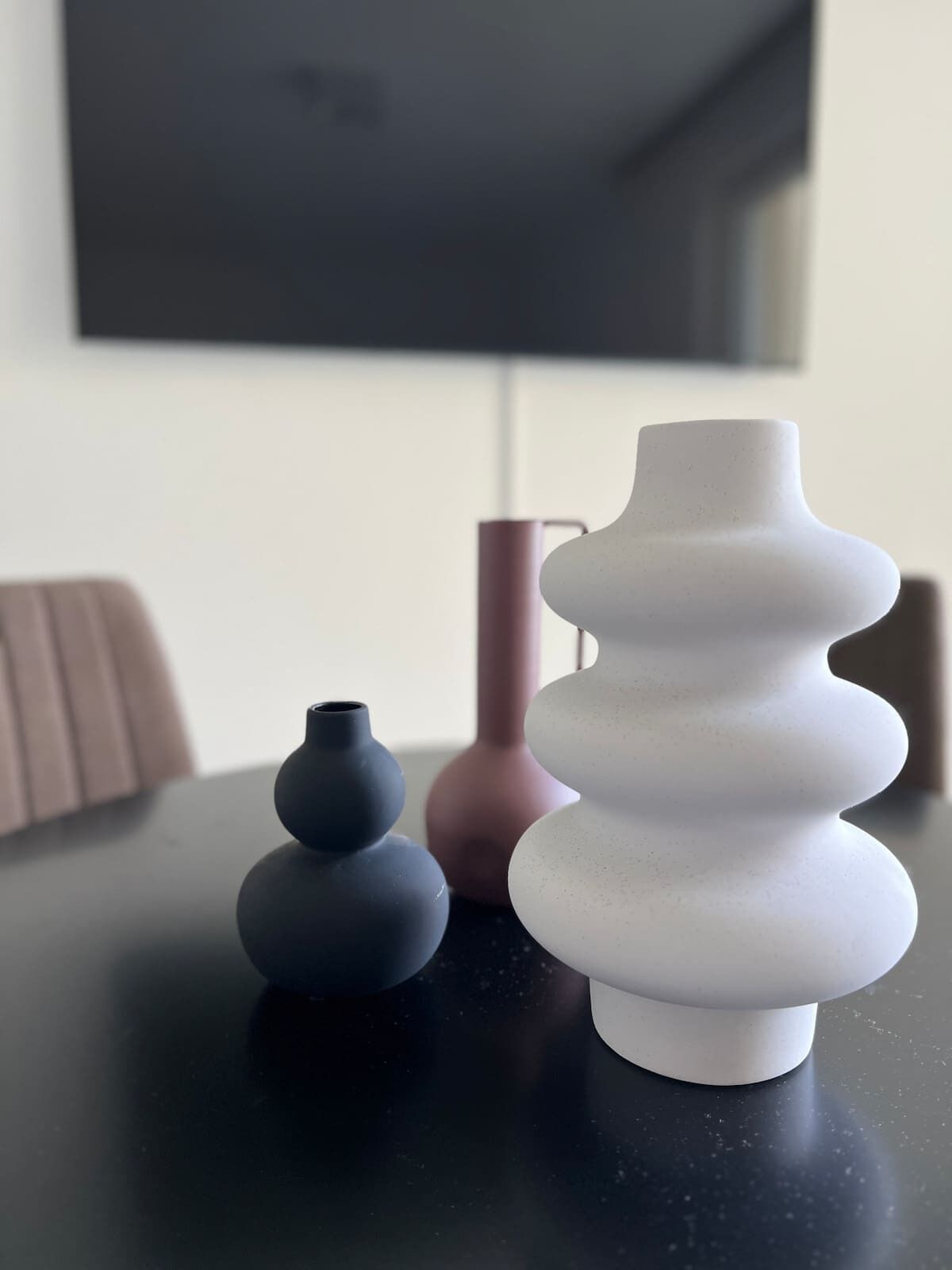 Three vases on a table with a modern interior, including a sofa and a flat-screen TV in the background.