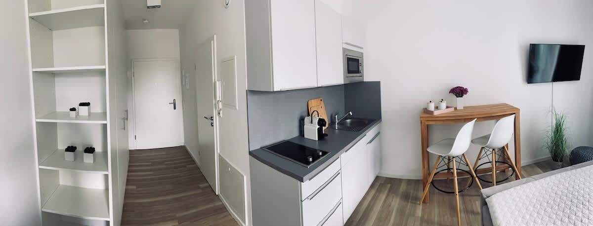 Une cuisine moderne avec des meubles blancs, un plan de travail noir et une table à manger en bois accompagnée de deux chaises.