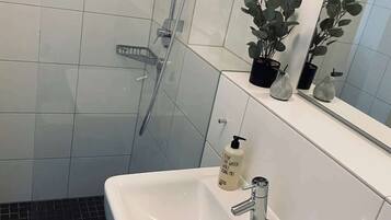 A bathroom with a white sink, a glass shower enclosure, a potted plant, and a mirror above the sink.