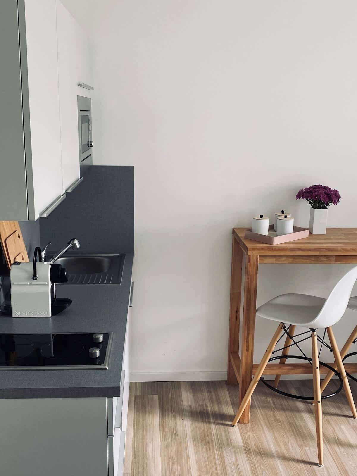 Una cocina moderna con una máquina de espresso integrada, una mesa de comedor de madera con una silla blanca y una pequeña planta en maceta.