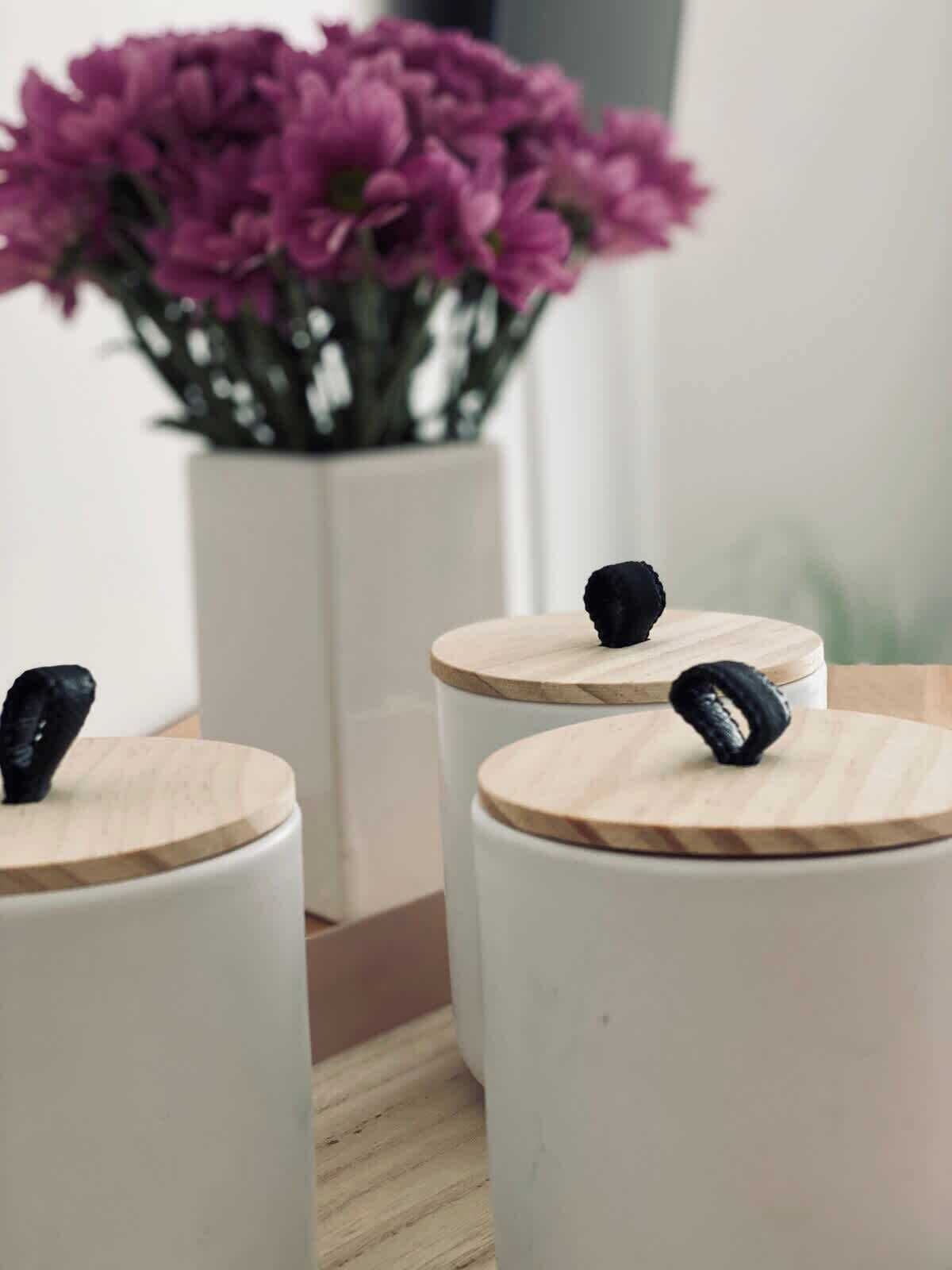 Three white cylindrical containers with wooden lids and black rubber bands on a wooden surface.