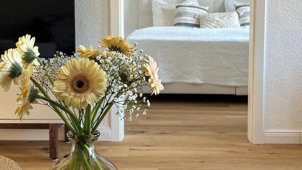 A room with a bed, a TV, and a vase of flowers on a table.