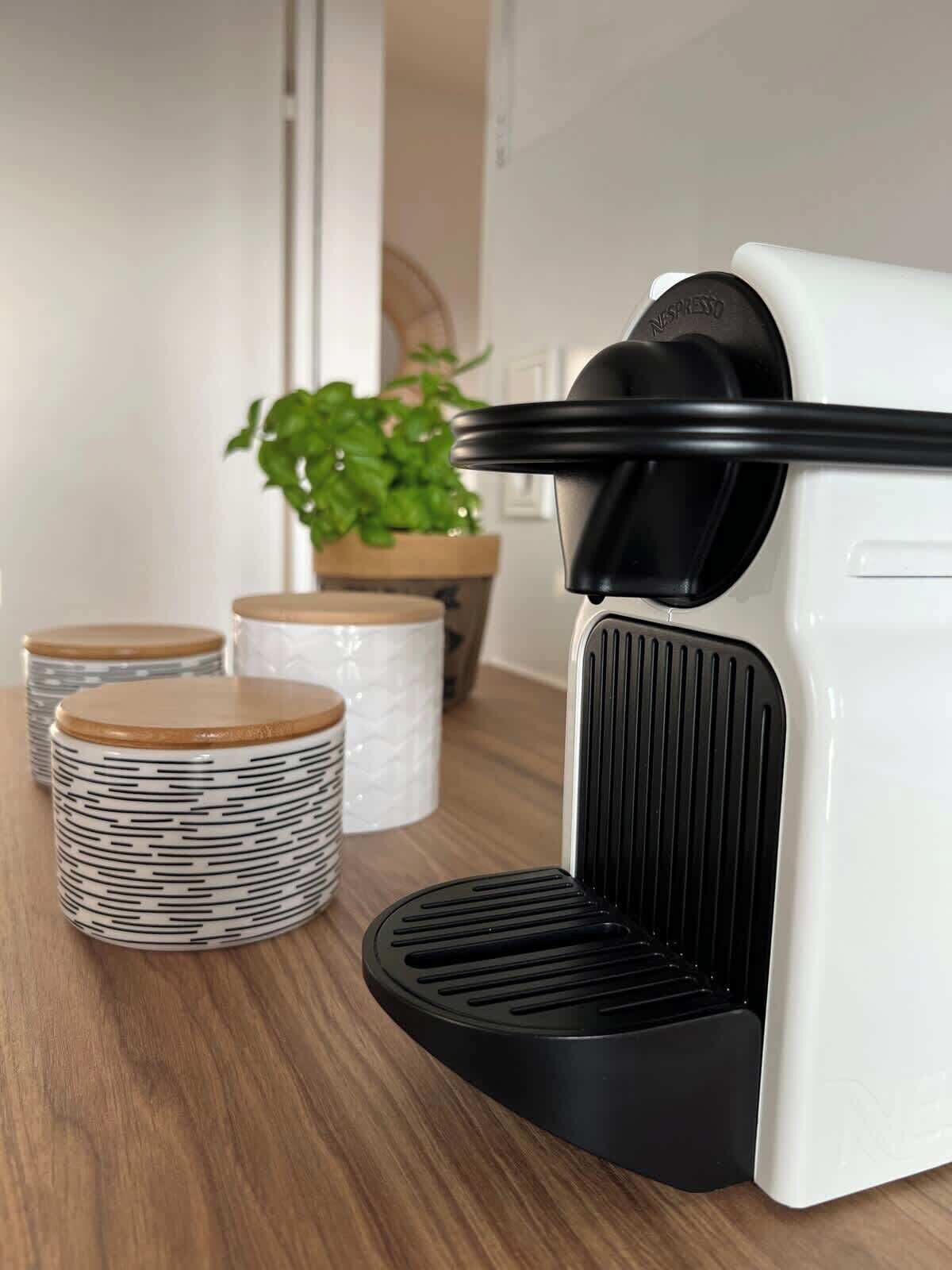 A coffee machine with a black and white design, a wooden plant in the background, and stacked containers with lids.