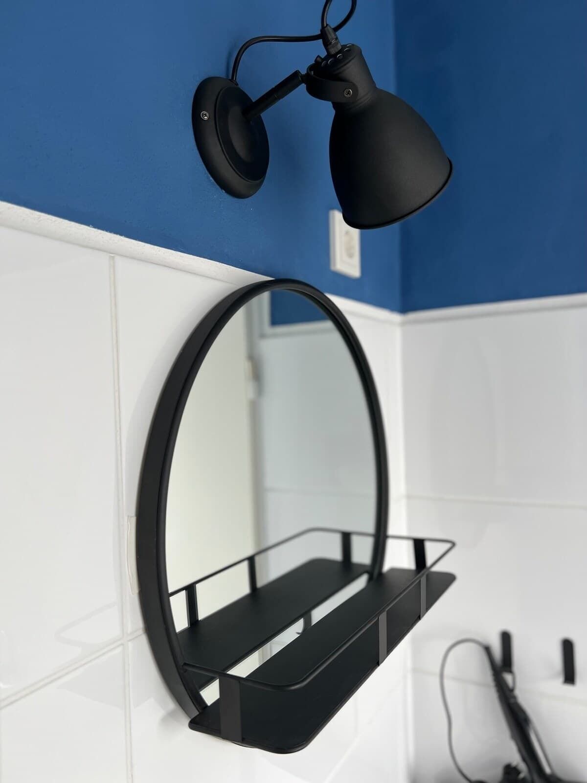 Une lampe de bureau noire à col flexible, fixée à un mur blanc orné d’une bordure bleue.