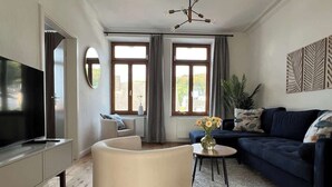 A modern living room with a flat-screen TV, a round white armchair, a dark blue sofa, and a coffee table with flowers.
