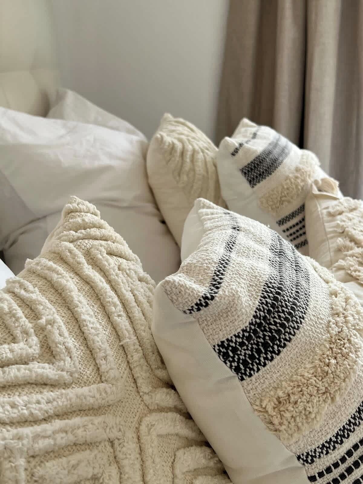 Un lit avec une couverture blanche à texture et deux oreillers, dont un uni et un à rayures.