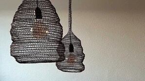 A dining table with a fruit bowl and two hanging woven light fixtures.