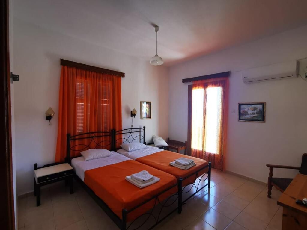 A bedroom with two beds, orange curtains, a ceiling fan, and a small table.