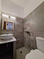 Un baño con lavamanos, espejo y inodoro blancos. Las paredes están cubiertas de azulejos con un diseño decorativo.