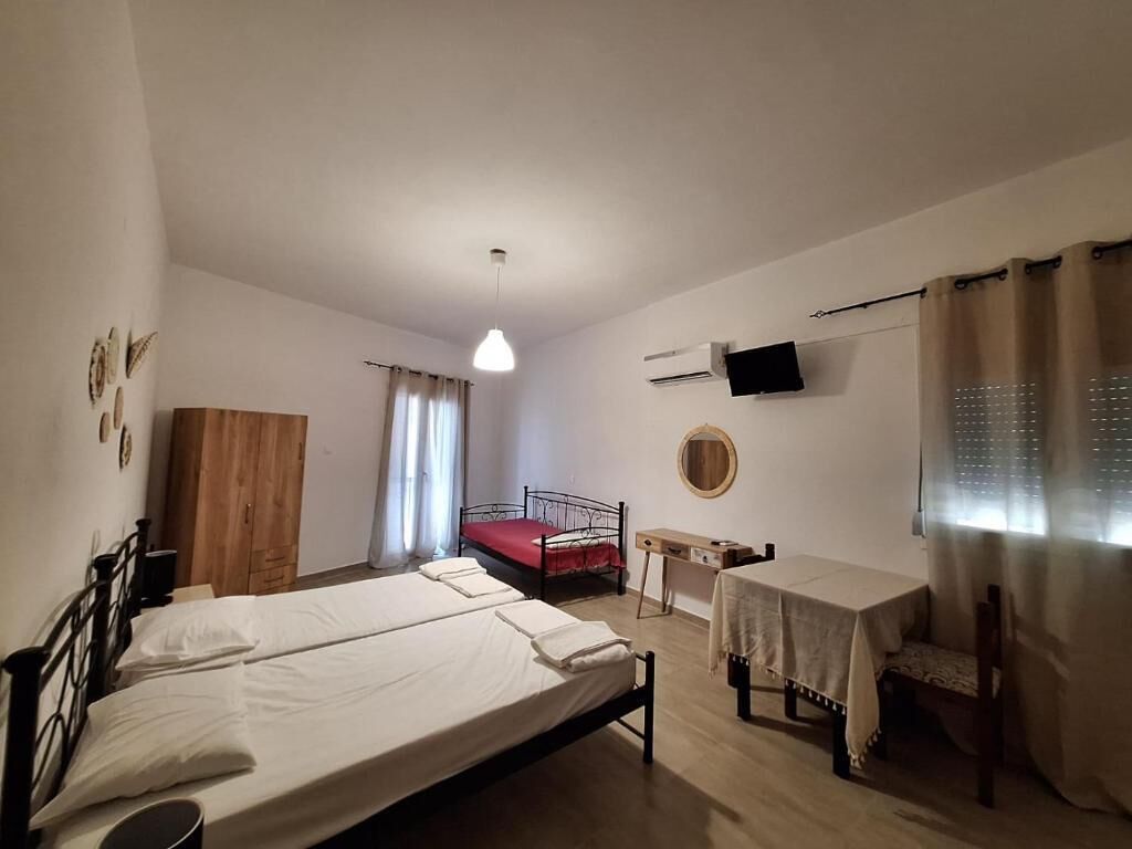 Una camera da letto con due letti, un armadio in legno, una scrivania, una televisione e una finestra con tende.