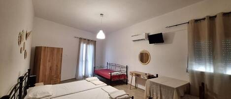 Una camera da letto con due letti, un armadio in legno, una scrivania, una televisione e una finestra con tende.