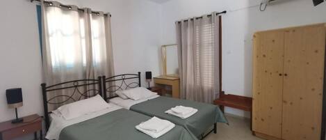 Un dormitorio con dos camas, un armario, una mesita de noche con lámpara y una ventana con cortinas.