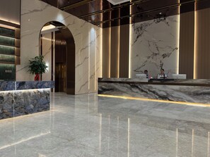 A modern lobby with marble flooring, a reception desk, and a large plant.