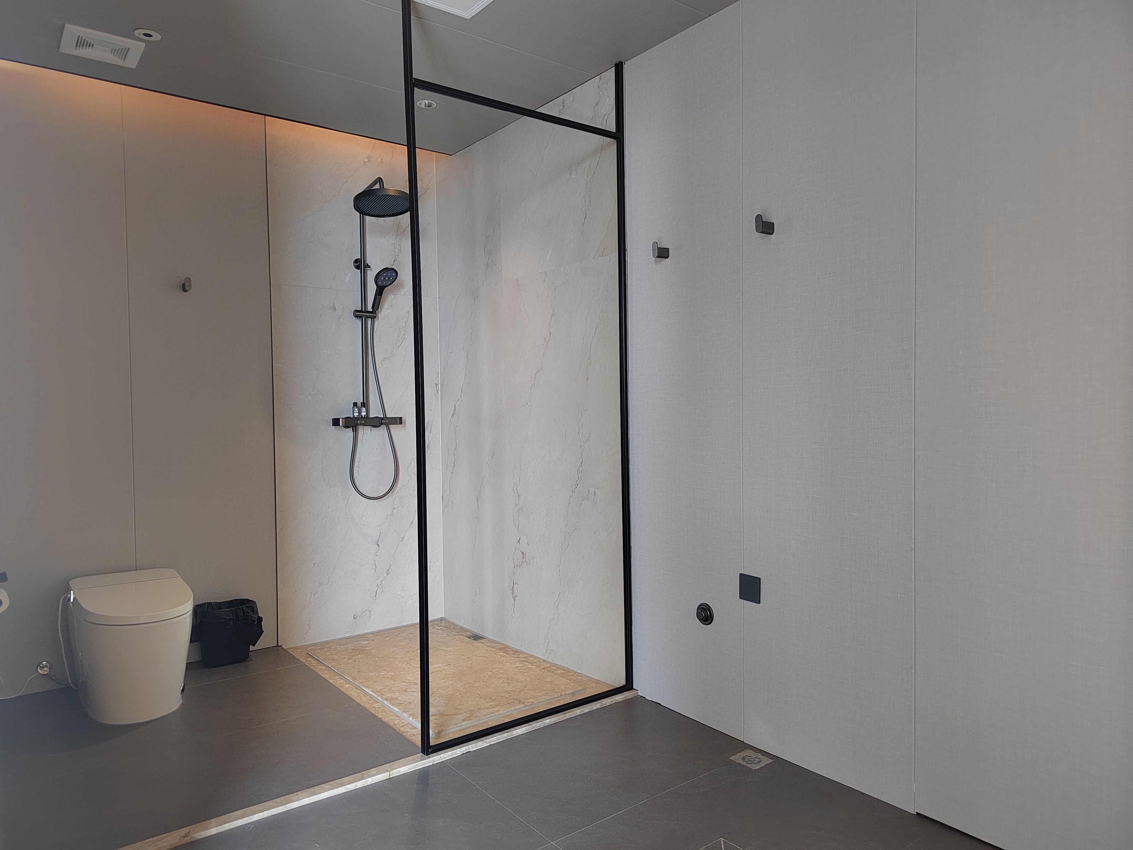 Un baño moderno con ducha envuelta en vidrio, inodoro y cubo de basura.