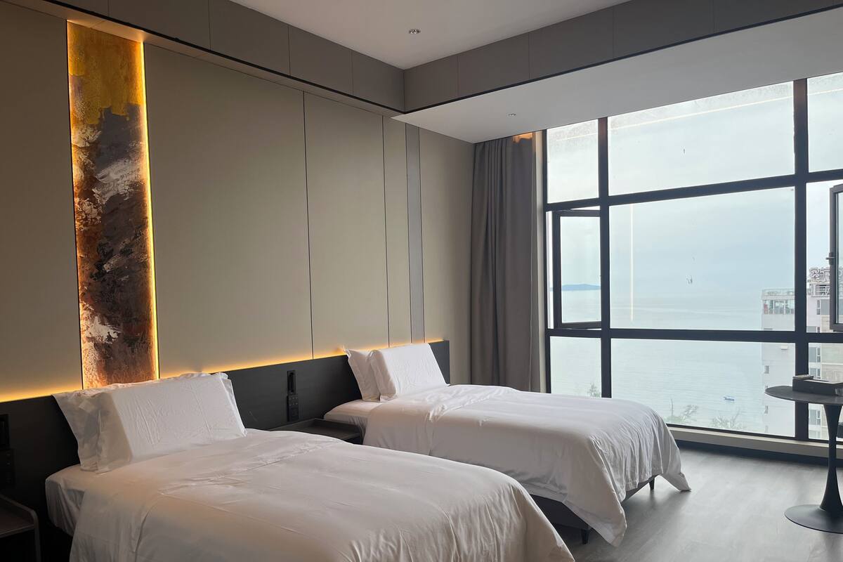 A hotel room with two beds, a large window with a view of the sea, and a modern design.