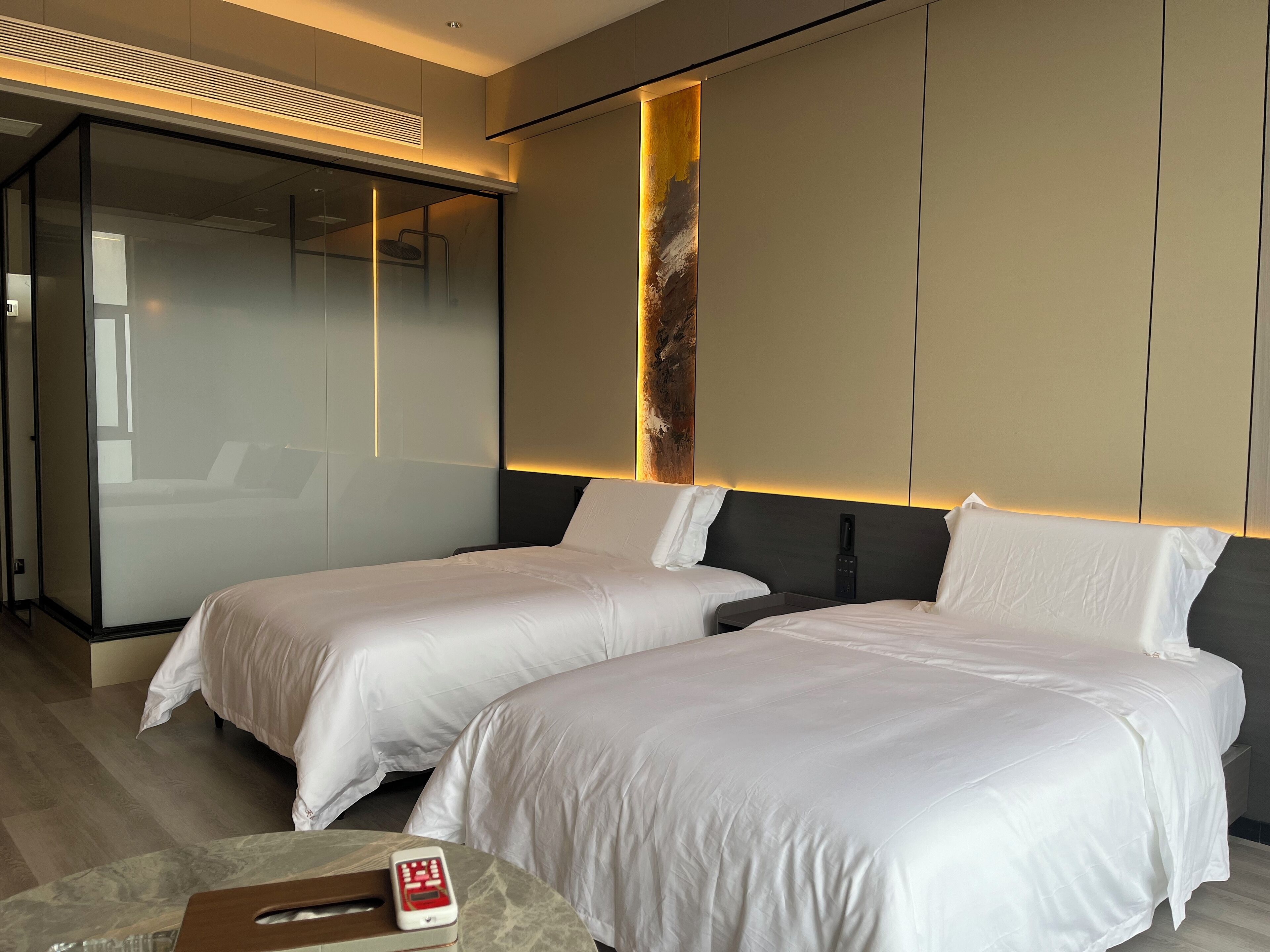 Una habitación de hotel moderna con dos camas, un separador de vidrio y suelo de madera.