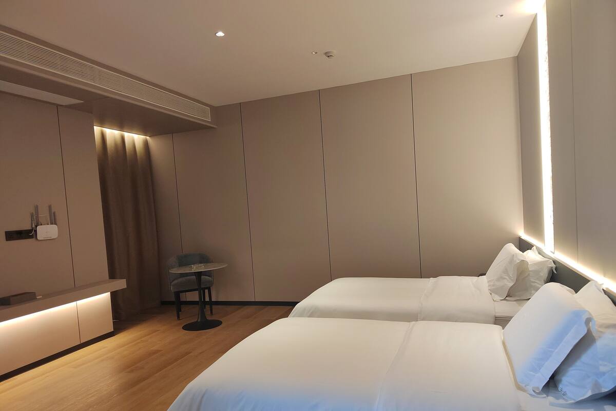 A modern hotel room with a large bed, bedside tables, a small round table, and a built-in shelf with a lamp.