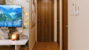 A hallway with a wooden floor, a TV mounted on a marble wall, and a wooden door at the end. - A.Venue Residences Suites Poblacion Makati (Makati City)