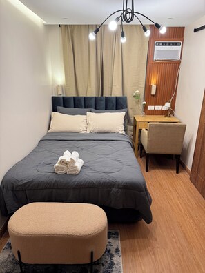 Ein ordentlich eingerichtetes Schlafzimmer mit Bett, Nachttisch, Sessel und einem kleinen Tisch mit einer Vase.