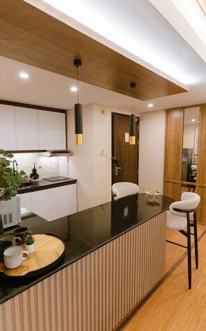 A modern kitchen with a black countertop, wooden ceiling, and pendant lights. - A.Venue Residences Suites Poblacion Makati (Makati City)