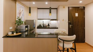 A compact kitchen with a central island, modern pendant lights, and a wooden door. - A.Venue Residences Suites Poblacion Makati (Makati City)