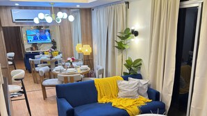 A modern living room with a blue sofa, a round coffee table, and a TV mounted on the wall. - A.Venue Residences Suites Poblacion Makati (Makati City)