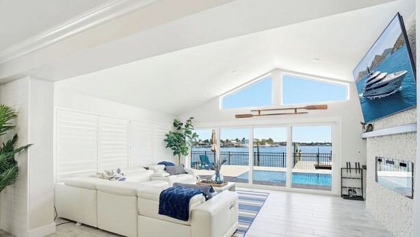 A spacious living room with a white sofa, a large window overlooking a pool and a yacht, and a high ceiling with skylights. - Yacht Club Waterfront Home 4BR + Den & Pool (Indian Rocks Beach)