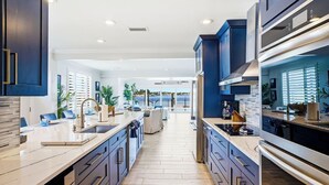 A modern kitchen with dark blue cabinets, a marble countertop, and a central island. - Yacht Club Waterfront Home 4BR + Den & Pool (Indian Rocks Beach)