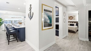A modern interior with a kitchen area, bar seating, and a bedroom. - Yacht Club Waterfront Home 4BR + Den & Pool (Indian Rocks Beach)