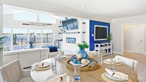 A spacious living area with a dining table set for six, a large TV, and a view of the outdoors. - Yacht Club Waterfront Home 4BR + Den & Pool (Indian Rocks Beach)