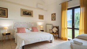 A bedroom with a bed, bedside tables, a chair, a window with curtains, and wall-mounted artwork. - Agriturismo il Montoto - Nature & Relax (Castiglione della Pescaia)