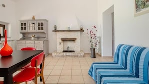 A living room with a fireplace, a dining table with red chairs, a sofa with blue stripes, and a kitchen area with cabinets and a countertop. - Agriturismo il Montoto - Nature & Relax (Castiglione della Pescaia)