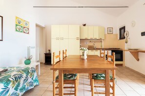 A modern kitchen with white cabinets, a wooden dining table, and a green plant.