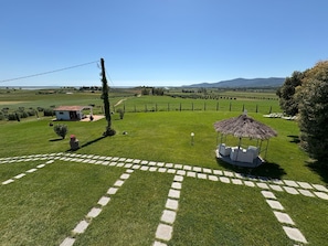 A grassy field with a gazebo, a small building, and a paved path.