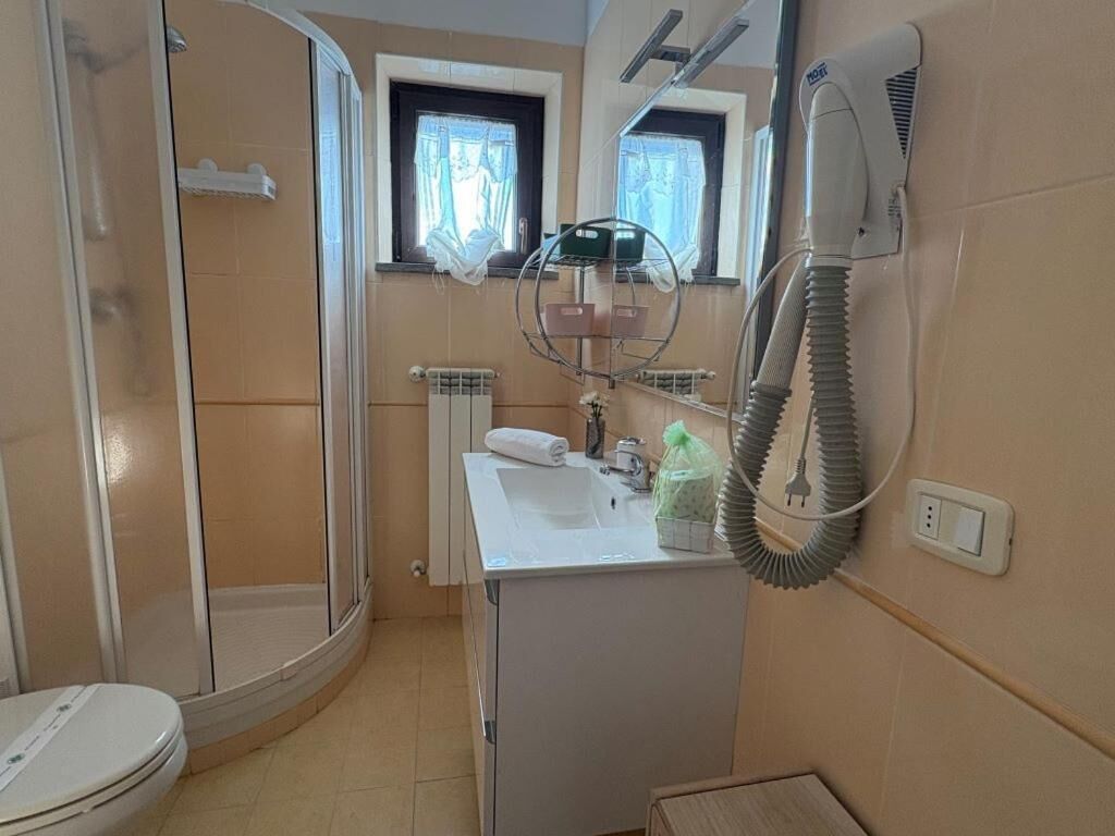 A bathroom with a shower, toilet, sink, and a hairdryer mounted on the wall.